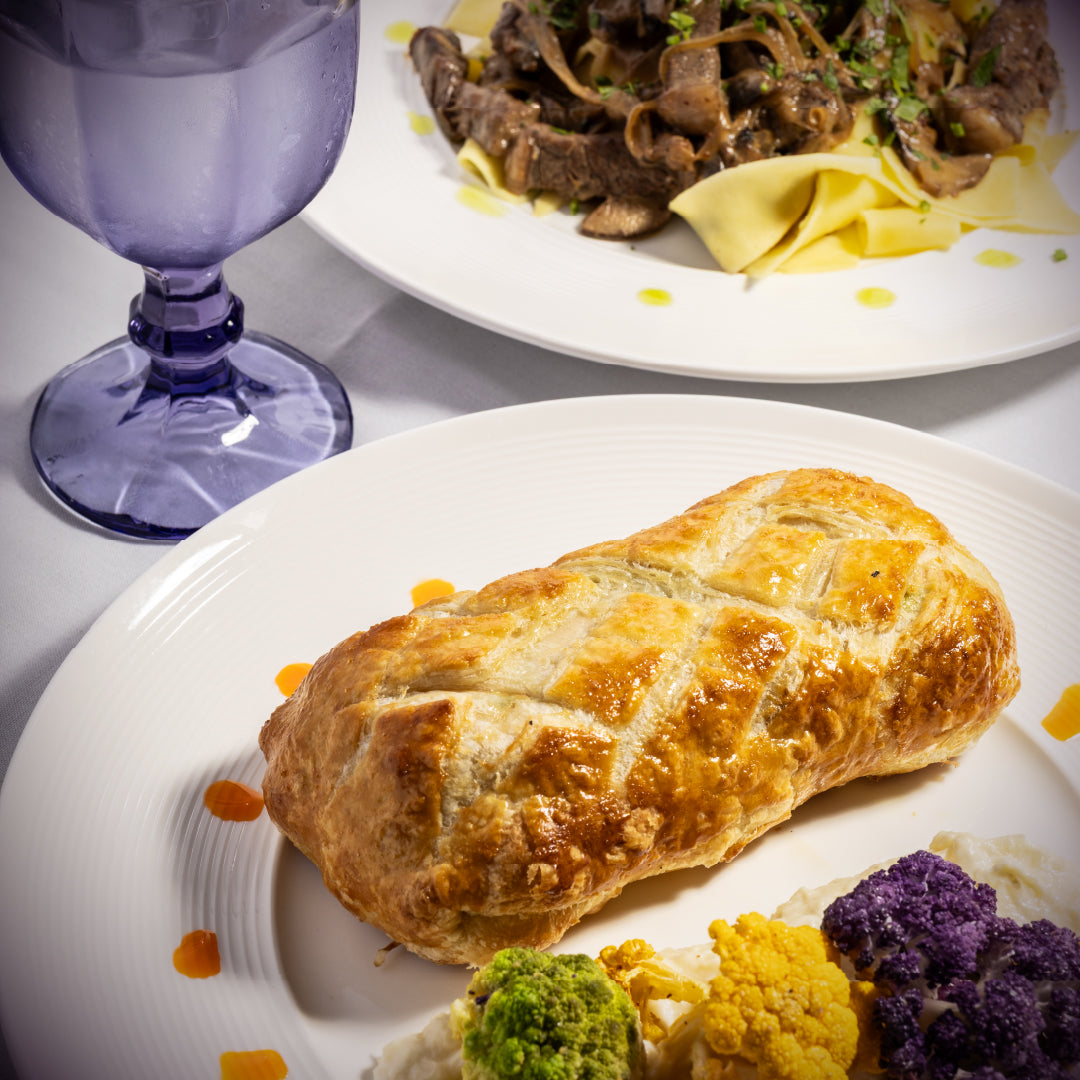 Baked dish on a plate with a side of vegetables and a purple glass in the background.