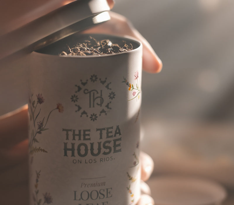 Tea tin with 'The Tea House on Los Rios' branding held by a hand in a beautiful morning lit tea room