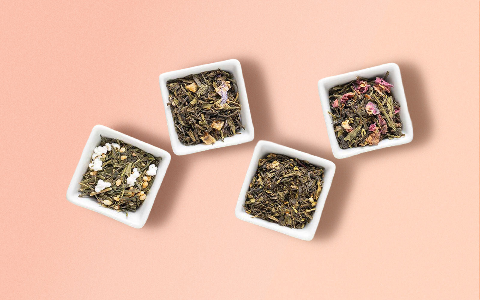 Four small white bowls filled with different types of green tea leaves on a pink background