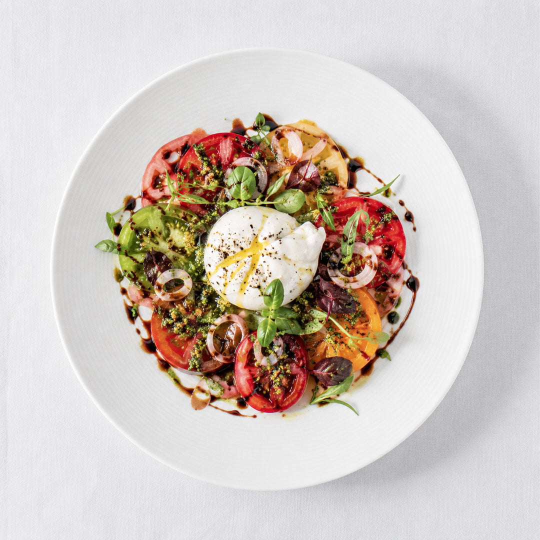 Plated dish with tomatoes, burrata, and herbs on a white background
