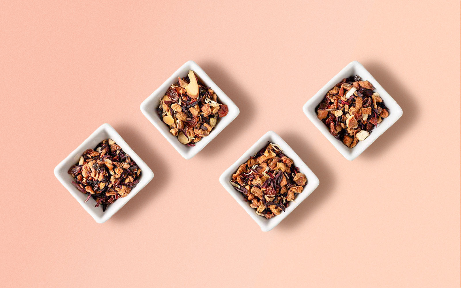 Four square white containers with different types of herbal tea on a pink background