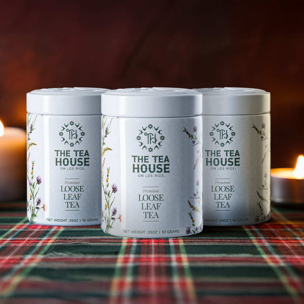 Three 'The Tea House' tea tins on a plaid tablecloth with candles in the background.