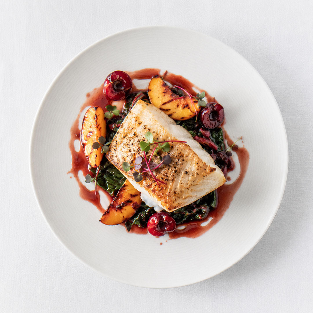 Plated dish with fish, peaches, and greens on a white background
