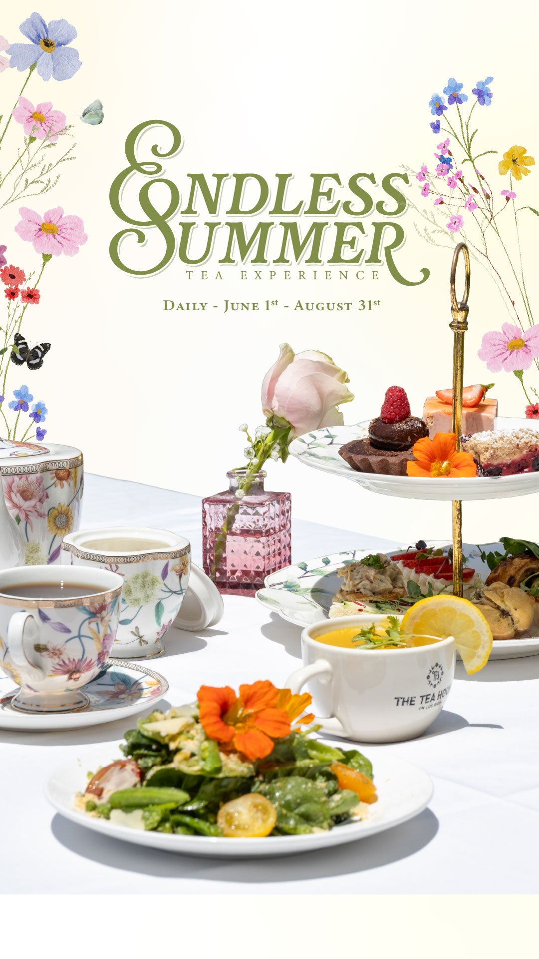 Tea party setup with tea cups, pastries, and flowers on a white tablecloth.