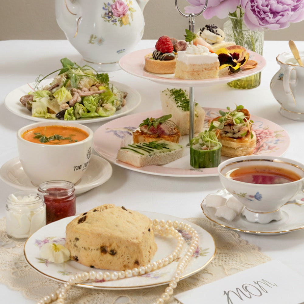 High tea set with sandwiches, tea, and a three-tiered cake stand on a table.
