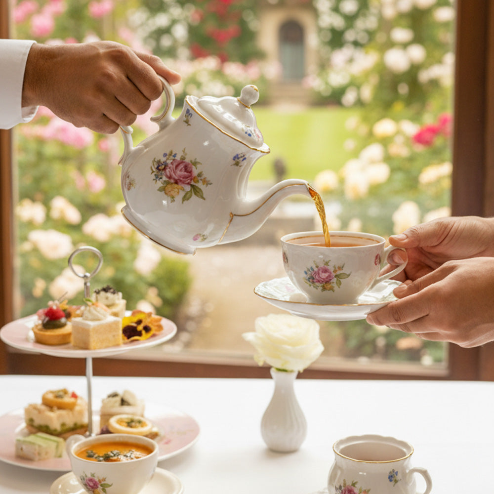 Tea being poured from a floral teapot into a cup with a garden view in the background