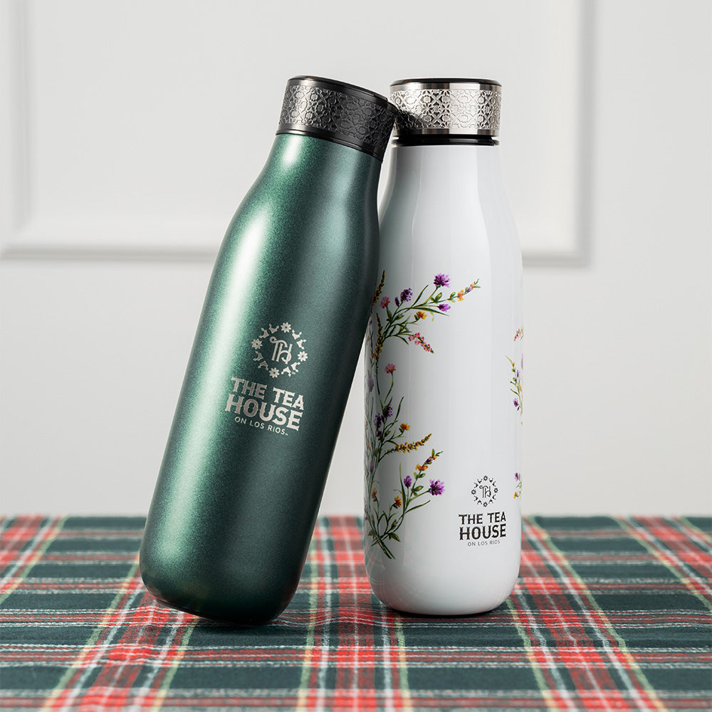 Two insulated bottles, one green and one white with floral design, on a plaid surface.