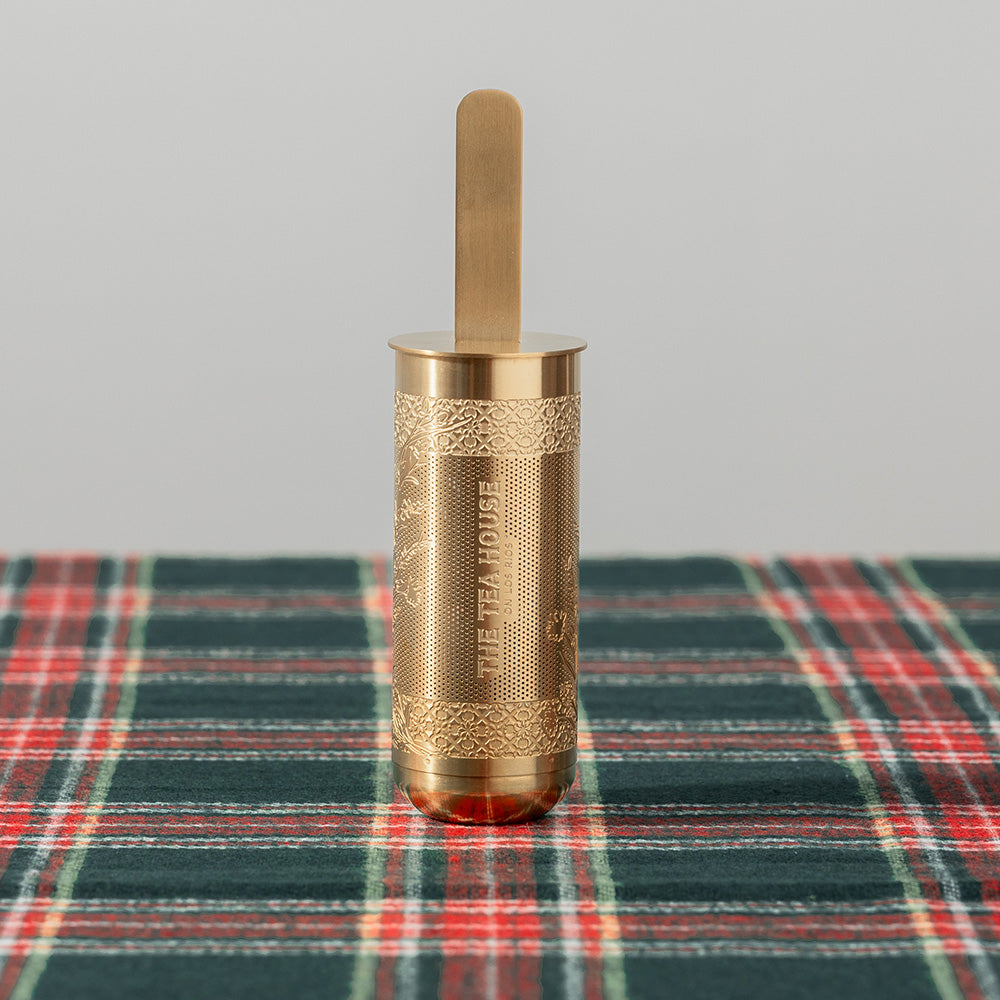 Brass tea infuser with decorative patterns on a plaid fabric background