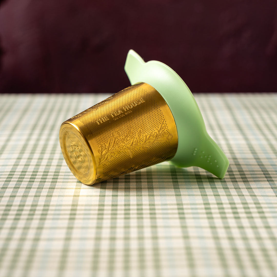 Gold and green tea infuser on a checkered tablecloth