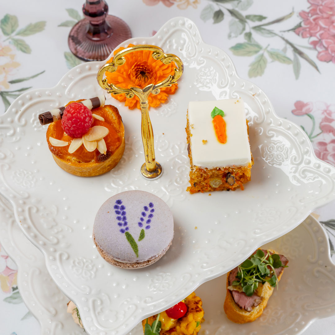 Assorted small desserts on a decorative white plate with a floral tablecloth.