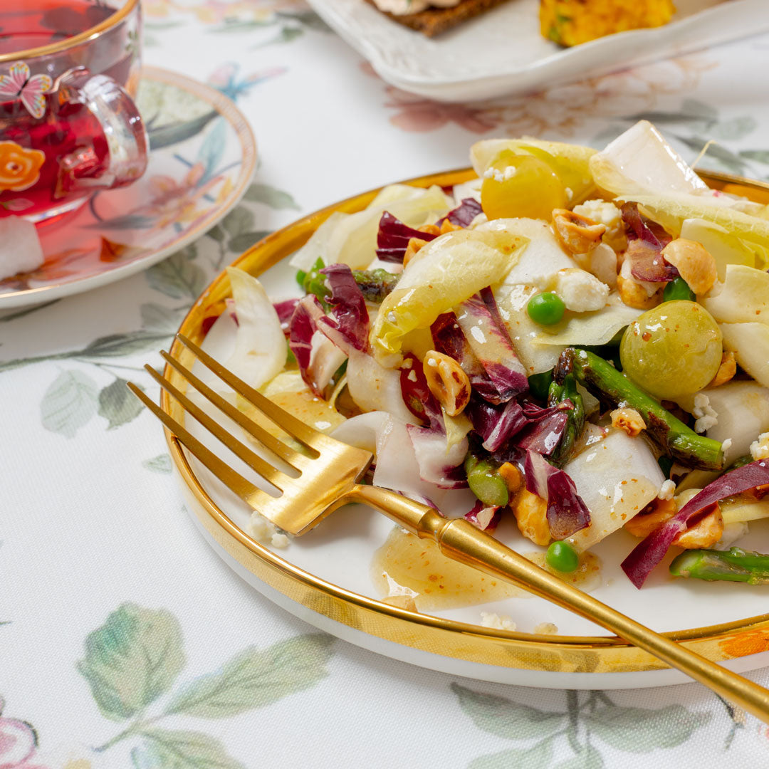 Colorful salad on a white plate with a gold fork, placed on a floral tablecloth.
