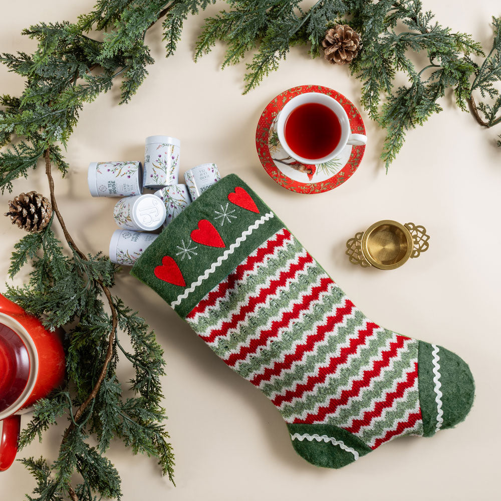 Decorative Christmas stocking with red and green patterns, surrounded by pine branches and a teacup.