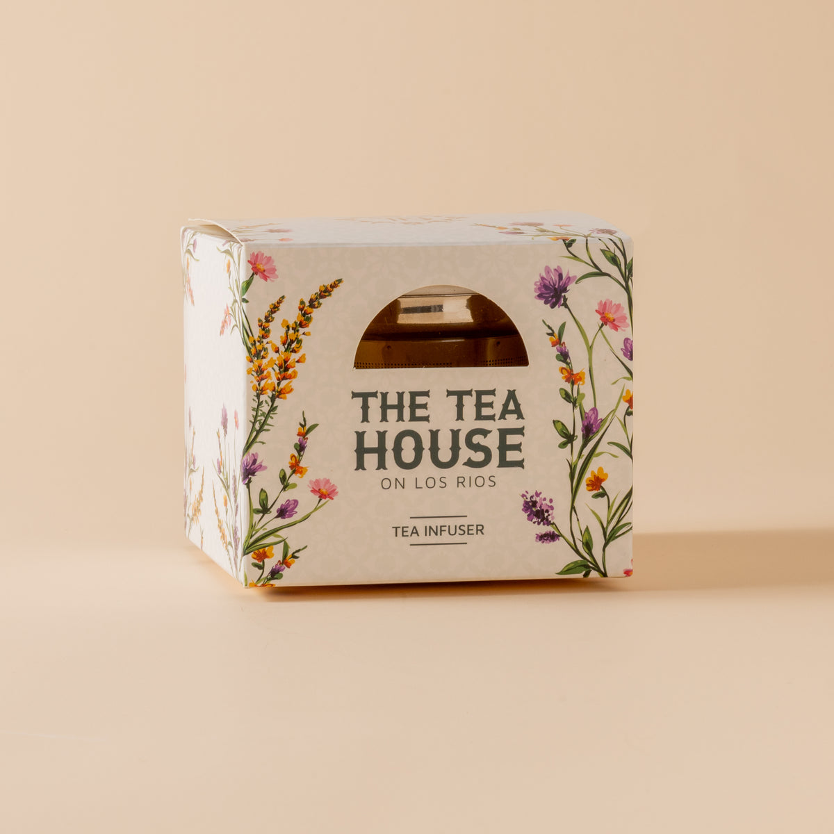 Tea infuser packaging with floral design and 'The Tea House on Los Rios' text on a beige background