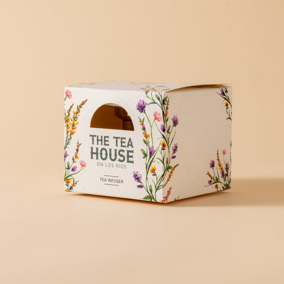 Tea infuser packaging with floral design and 'The Tea House' branding on a beige background