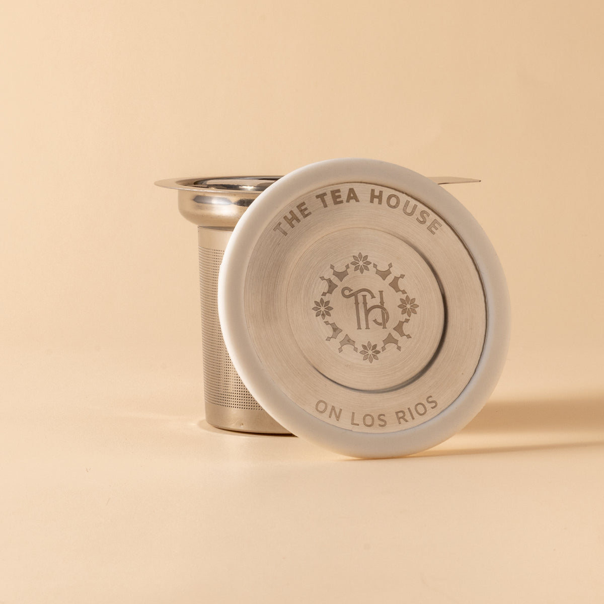 Tea infuser with 'The Tea House on Los Rios' branding on a beige background