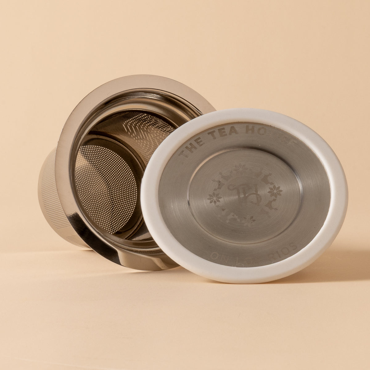 Metallic tea infuser with brand logo on a beige background