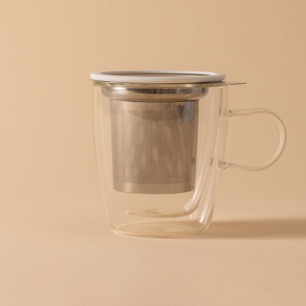 Clear glass tea mug with metal infuser on a beige background