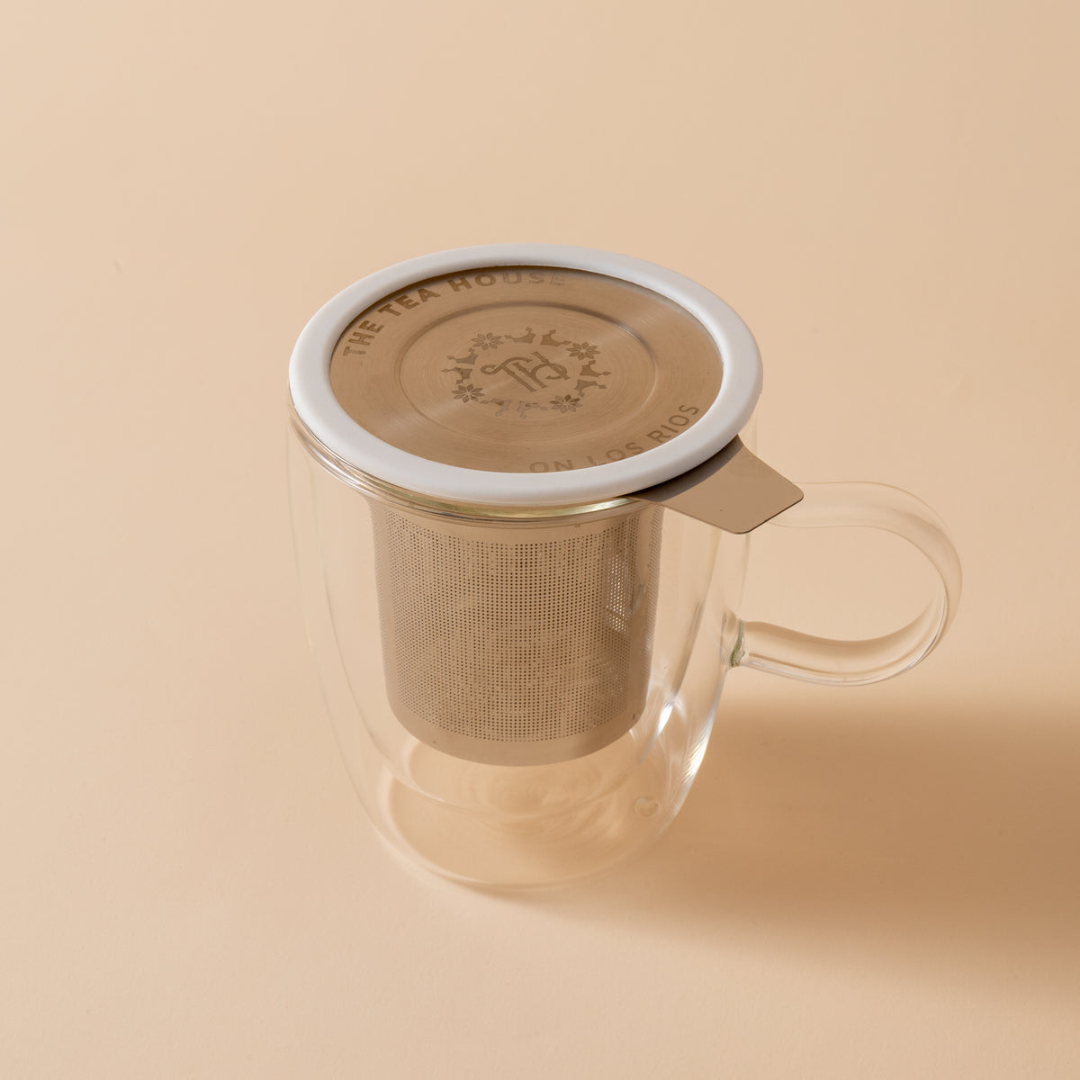 Clear glass mug with metal tea infuser on a beige background
