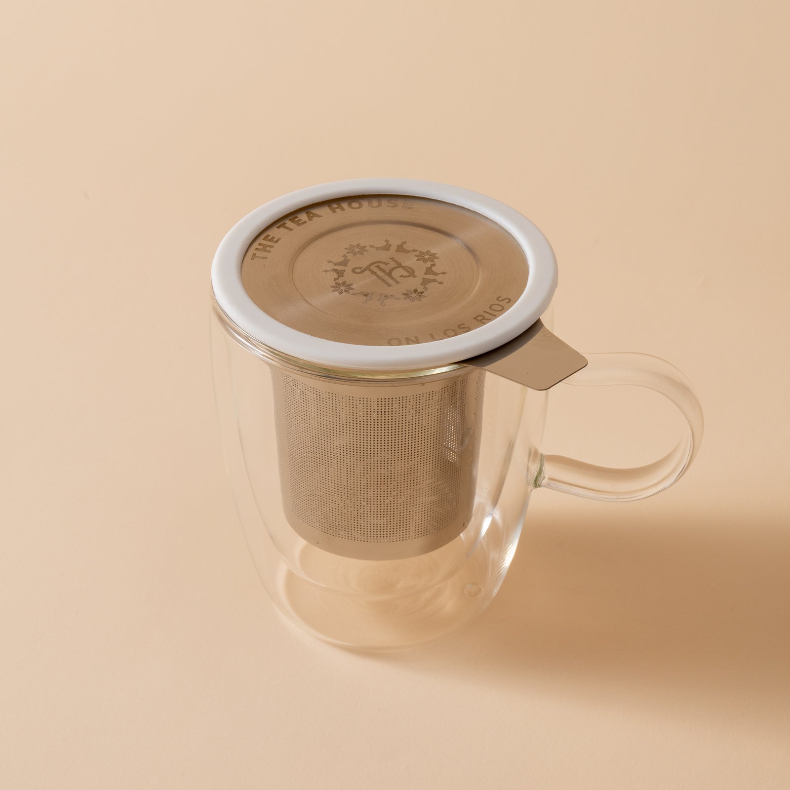 Clear glass mug with metal tea infuser on a beige background