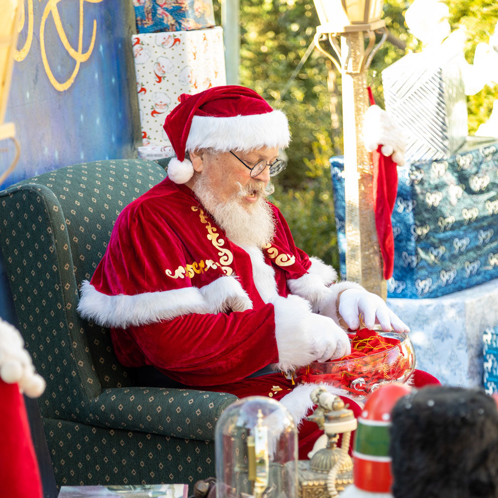 Man in Santa Claus costume sitting on a green chair with Christmas decorations around.
